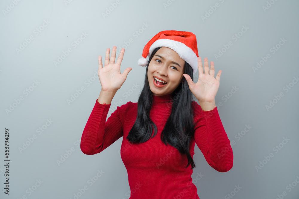 Pretty lovely lady asian thai women in red sweater and santa christmas hat isolated over grey background. hand wave Pretty lovely lady asian thai women in red sweater and santa christmas hat isolated over grey background. hand wave