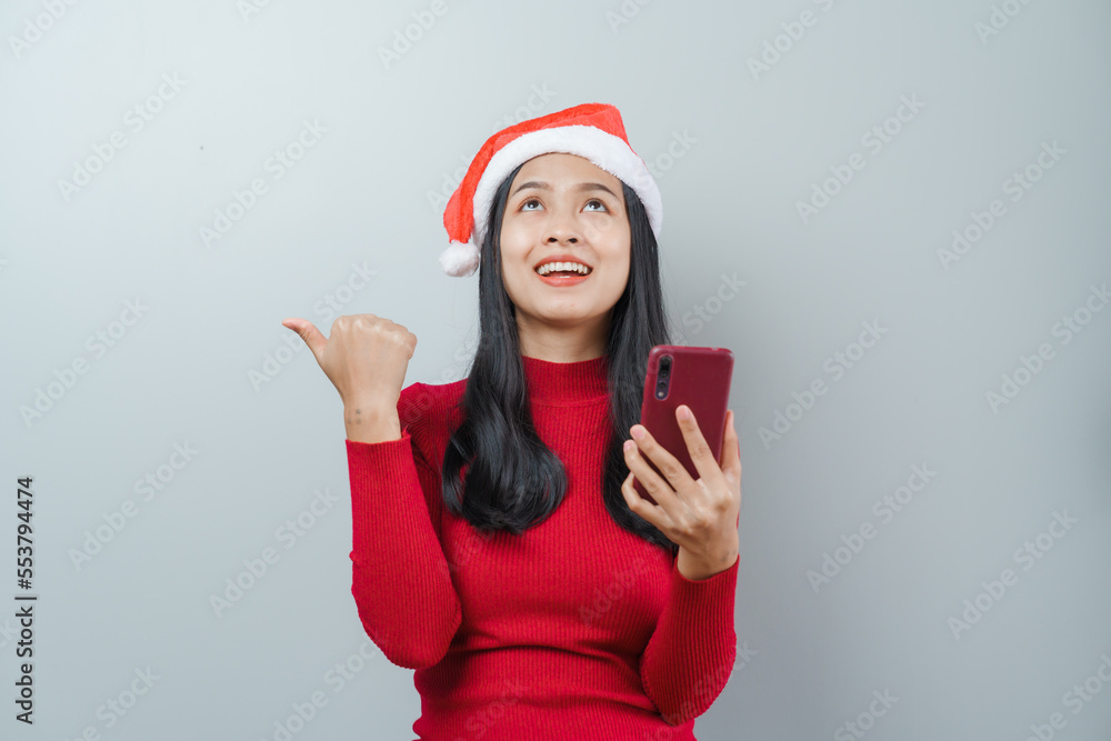 Pretty lovely lady asian thai women in red sweater and santa christmas hat isolated over grey background. Holding and using mobile smartphone or cellphone Pretty lovely lady asian thai women in red sweater and santa christmas hat isolated over grey background. Holding and using mobile smartphone or cellphone