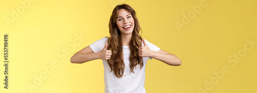 Outgoing positive confident lively young girl long curly haircut support great effor show thumbs up positive reply approving good choice like your outfit smiling broadly yellow background photo