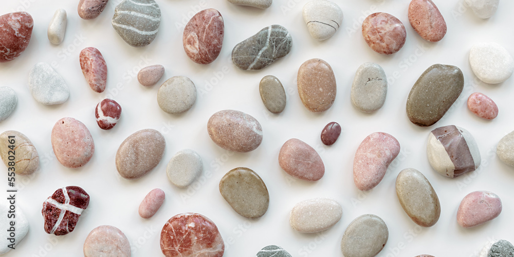 Top view close up sea stones on light background. Colorful pebbles as summer pattern. Natural stone white red pink grey colors. Minimal flat lay, banner with natural materials
