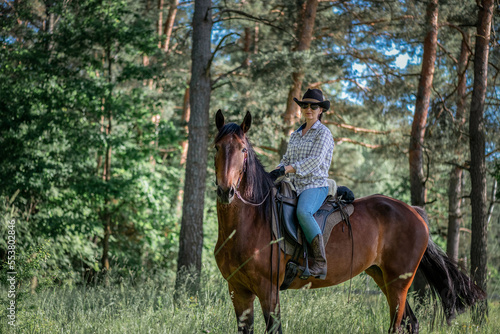 Portrait of a young beautiful girl in a cowboy hat on a horse in the forest. © shymar27