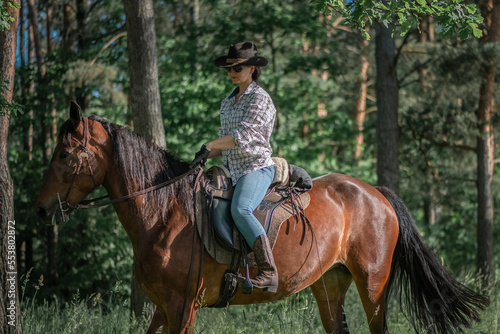 Portrait of a young beautiful girl in a cowboy hat on a horse in the forest.