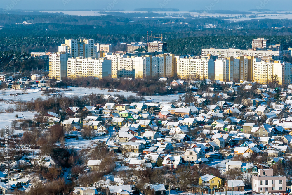 panoramic aerial view of a winter city with a private sector and high-rise residential areas with snow