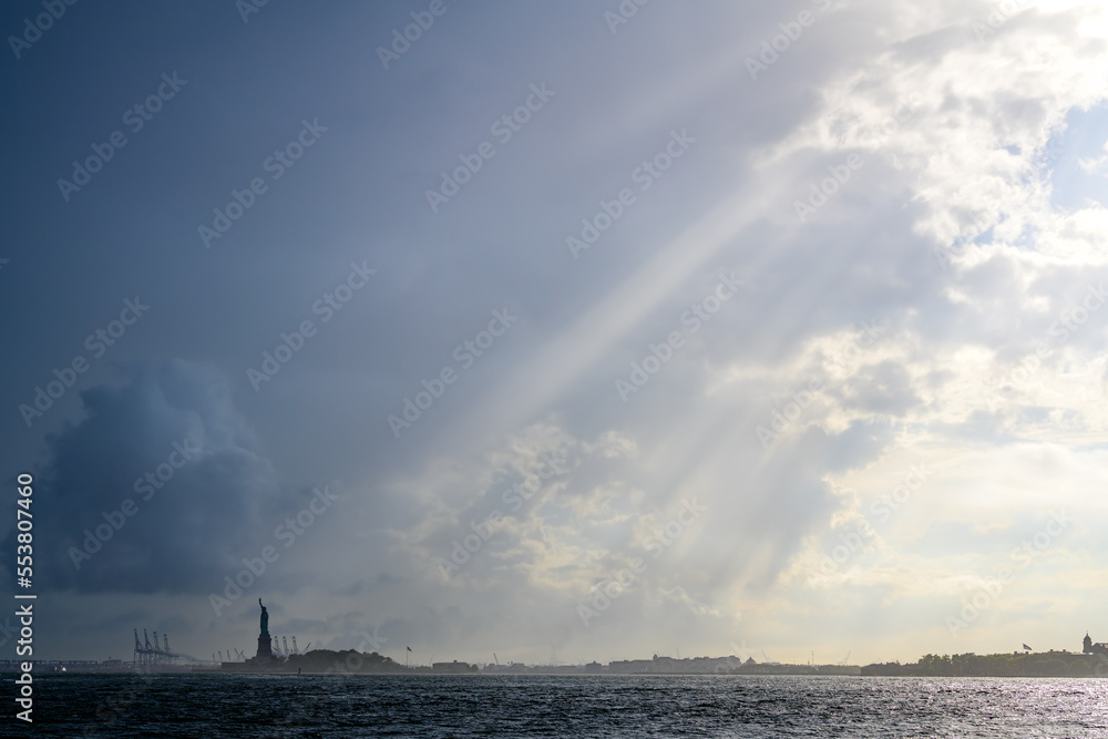 The Statue of Liberty lighten by sun rays in a cloudy day in New York City.