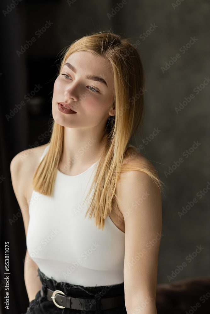 Blonde woman in white top looking away at home. Blonde woman in white top looking away at home.