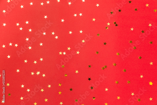 Gold sparkle confetti stars on a red background. Glitter, shine, bright. Christmas festive flat lay, winter holiday, new year, happy birthday concept. Flat lay, top view, copy space.