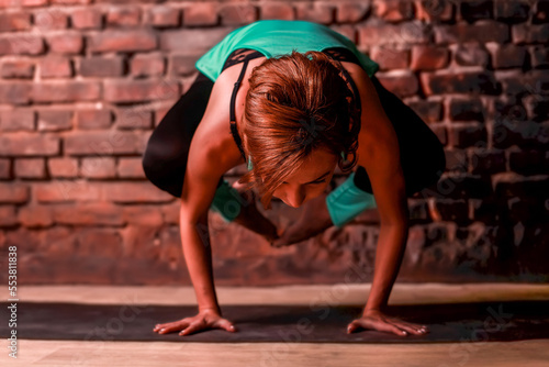 A young slender girl in black leggings and a birch T-shirt sits in an asana against the background of a brick wall.