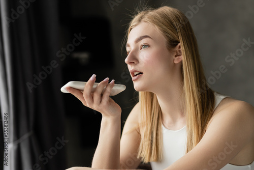 Foto Blonde woman recording voice message on smartphone at home.