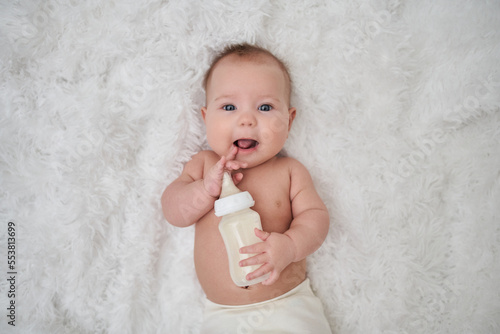 portrait of an infant lying on its stomach on a soft down blanket looking into the camera with a bottle of milk
