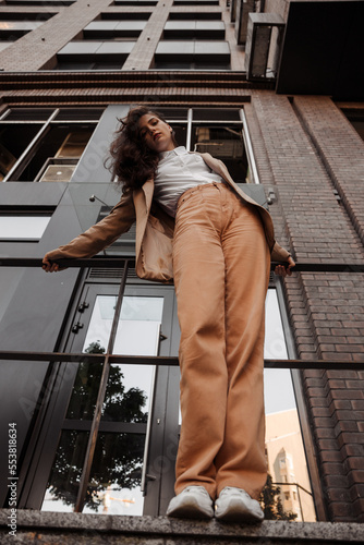 Tall stylish girl with oversized jacket posing near the railing and steps on the city background photo