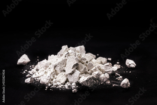 Calcium Chloride flakes, salt in solid state, used in brine for refrigeration machines, road dust and ice control, in cheese and in cement. Industrial use, isolated black background, copyspace