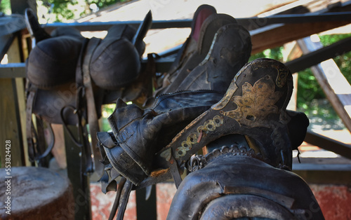 Traditional leather horse saddles hanging over wooden fences at a horse farm
