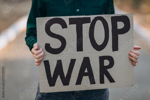 Ukrainian girl protests war, holds banner, placard with inscription message text Stop War, street background. Crisis, peace, stop aggression, against Russian invasion concept. anti-war demonstration.