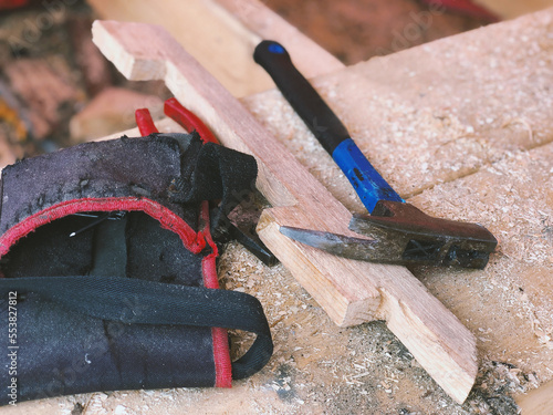 Metal blue hammer, black bag and red pliers lie in sawdust on wooden boards on the roof in focus close-up photo