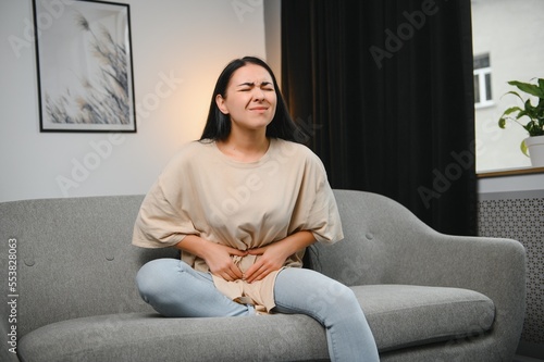 Εκτύπωση καμβά young beautiful hispanic woman in painful expression holding her belly suffering menstrual period pain lying sad on home bed having tummy cramp in female health concept