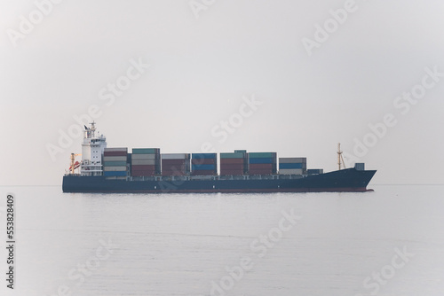 Cargo freight ship with containers and trucks sailing to industrial logistic port.