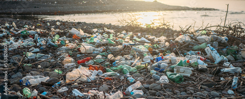  Stone beach with plastic waste. Plastic bottles in nature. Environmental pollution concept.