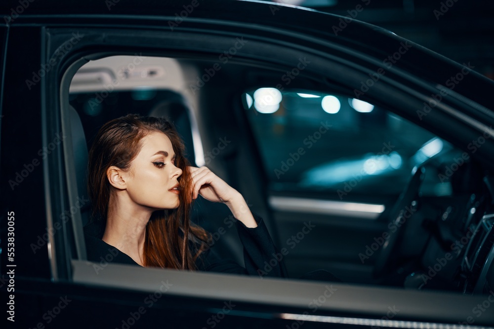 a stylish, luxurious woman is sitting in a black car at night, straightening her long, styled hair