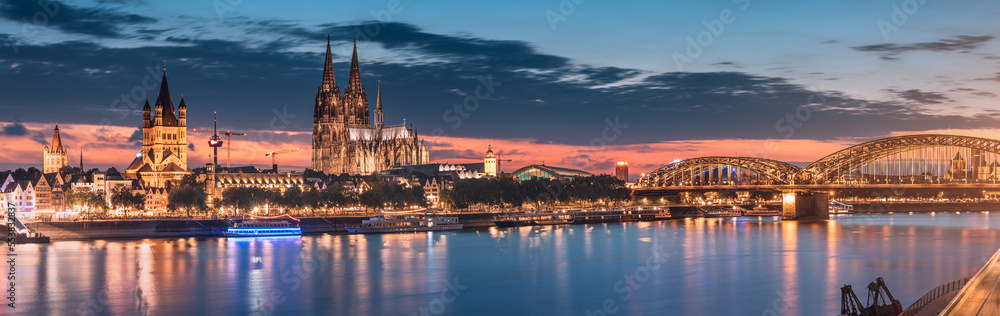 Cityscape night panoramic view of illuminated Cologne or Koln city with Cathedral Dom and bridge over Rhine river. Travel landmarks and sights