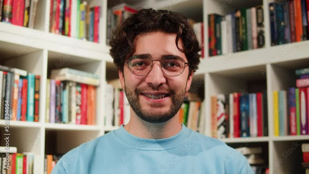 Man reading Book in University Library, Book Shop or Store, Spanish Student Wearing Glasses Standing near Bookshelf Reads Book and Exam Preparations. Man reading Book in University Library, Book Shop or Store, Spanish Student Wearing Glasses Standing near Bookshelf Reads Book and Exam Preparations.
