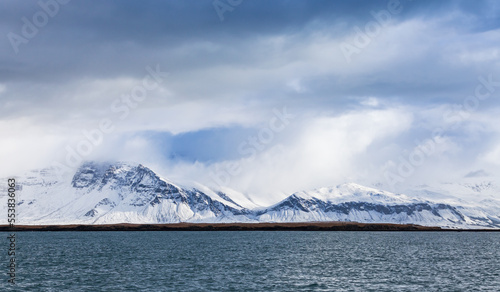 Winter coastal landscape with snowy mountains under cloudy sky