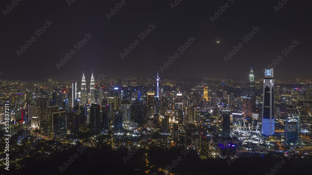 Aerial high angle night view time lapse overlooking busy city streets and a moon setting against a city skyline in Kuala Lumpur, Malaysia. Prores 4KUHD Timelapse. Aerial high angle night view time lapse overlooking busy city streets and a moon setting against a city skyline in Kuala Lumpur, Malaysia. Prores 4KUHD Timelapse.