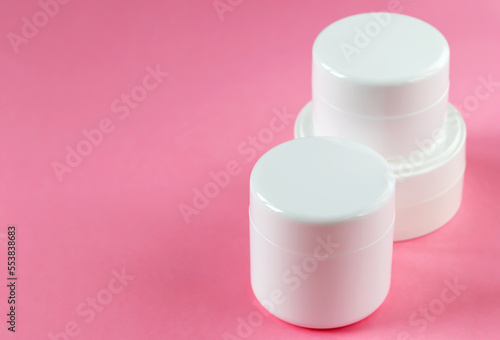 Three round cosmetic jars on a pink background