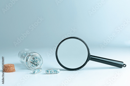 Medical pills and a magnifying glass on a blue background with a copyspace