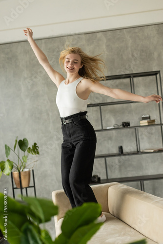excited woman with closed eyes and outstretched hands dancing on sofa at home.