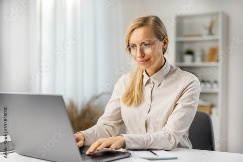 Attractive woman in eyeglasses working on laptop frm home, teacher having remote lesson, distant education. photo