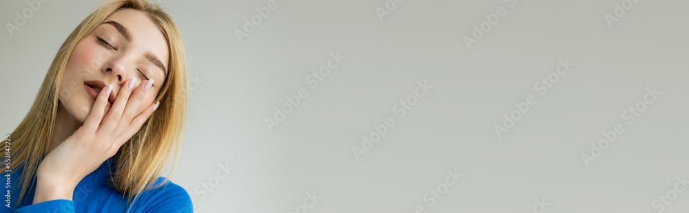 blonde woman with closed eyes holding hand on face while posing isolated on grey, banner. blonde woman with closed eyes holding hand on face while posing isolated on grey, banner.