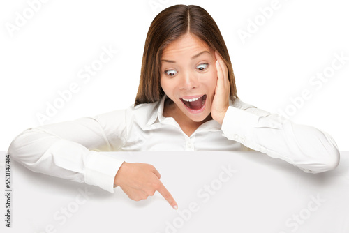 Advertising banner sign - woman excited pointing looking down on empty blank billboard paper sign board. Young business woman isolated cutout PNG on transparent background.