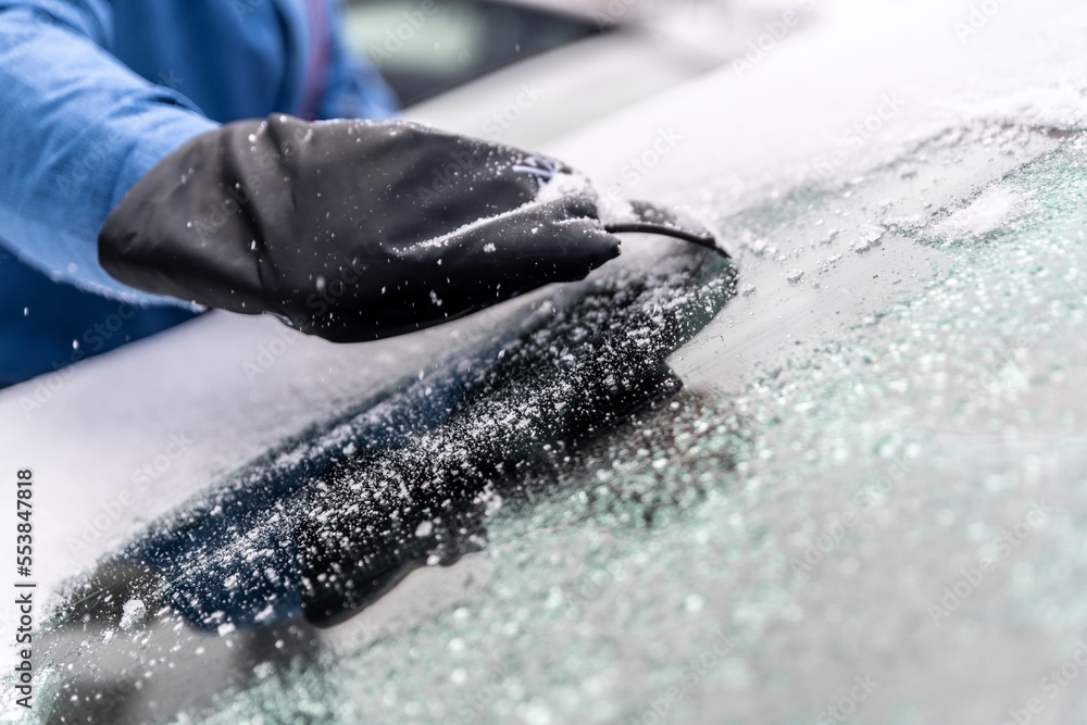 man uses ice scrapers to thaw an ice-covered car windshield