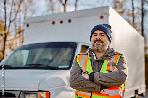 Portrait of happy professional truck driver with crossed arms looking at camera.