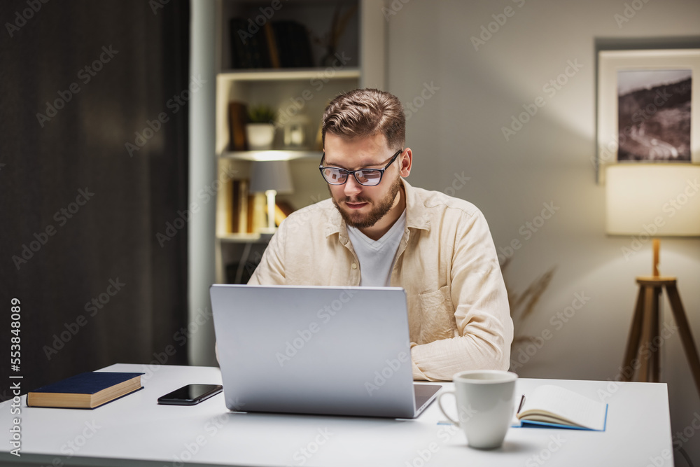 Male sitting at desk with laptop and sgtretching, trying to relax after work, feeling happy with job done Male sitting at desk with laptop and sgtretching, trying to relax after work, feeling happy with job done
