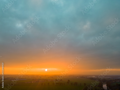 Aerial view of endless lush pastures and farmlands of Belgium under a dramatic colorful sunset sky. Beautiful antwerp countryside with emerald green fields and meadows. Rural landscape on sunset. High