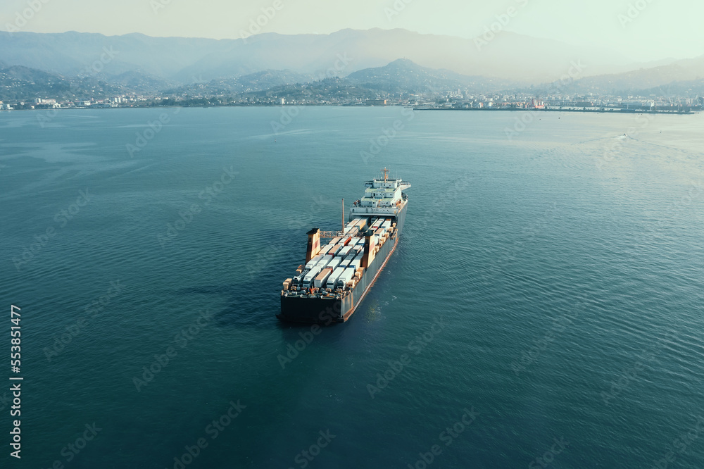 Cargo freight ship with containers and trucks, aerial view from drone. International global delivery and logistic business concept.