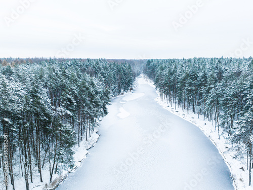 Aerial view of a frozen lake, a pond in the middle of the forest. The concept of a winter landscape, a beautiful view of a winter forest and a pond recorded from a drone.