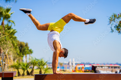 young man man performing dance movement standing on hand outdoors in sunny beach