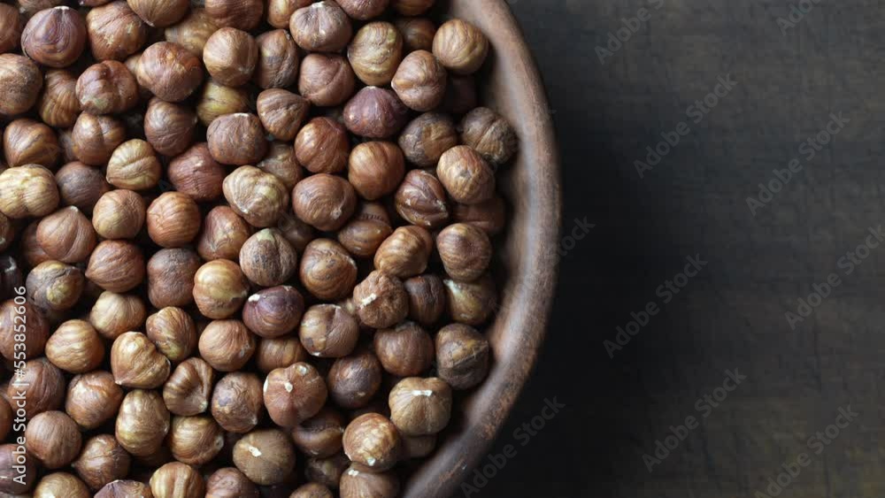 Dry hazelnuts in a ceramic plate rotate on a wooden background. Heap of peeled hazelnuts kernels, top view, close up, copy space for text Dry hazelnuts in a ceramic plate rotate on a wooden background. Heap of peeled hazelnuts kernels, top view, close up, copy space for text