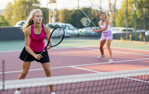 Sporty teenager girl player hitting ball with racket on court during friendly doubles couple match