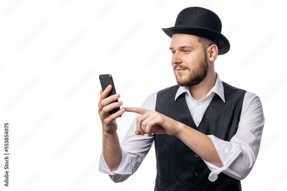 Man in funny old-fashioned hat, black waist and white shirt holding smartphone and smiling isolated on white background