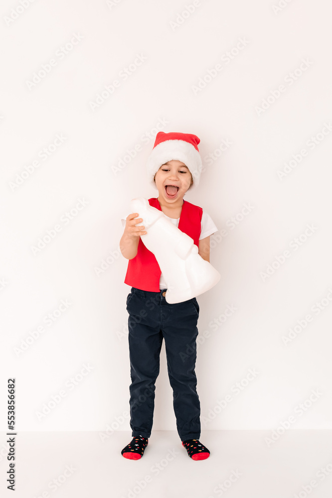 WOW. Portrait of standing child in red Santa Claus hat holding gift toy. Cute 5 year European happy boy. Isolated on white background. Vertical. Copy space. Christmas and New Year holidays concept WOW. Portrait of standing child in red Santa Claus hat holding gift toy. Cute 5 year European happy boy. Isolated on white background. Vertical. Copy space. Christmas and New Year holidays concept