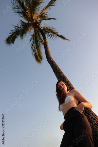 Jolie jeune femme se promenant au coucher du soleil sur une plage de Martinique en pantalon de costume et maillot de bain