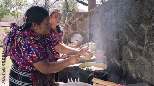 Madre e hija con un vestido colorido de la region cocinan juntas un platillo tradicional en estufa de leña.  photo