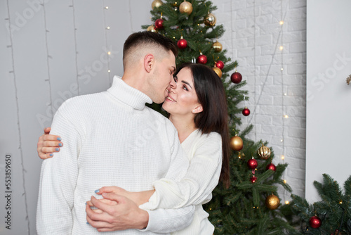 pretty couple in love kissing in christmas eve near tree with gifts at home in december. © Ryzhkov Oleksandr