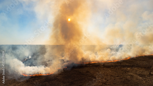 Field in countryside on fire at clear spring day, orange flames and smoke in the air. Natural catastrophe, agricultural damage, danger