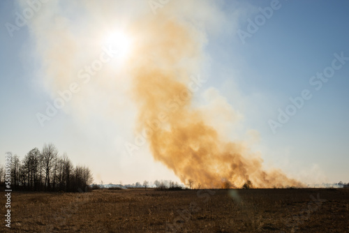 View on spring field, dry grass, orange smoke on horizon. Nature on fire, agricultural damage and air pollution