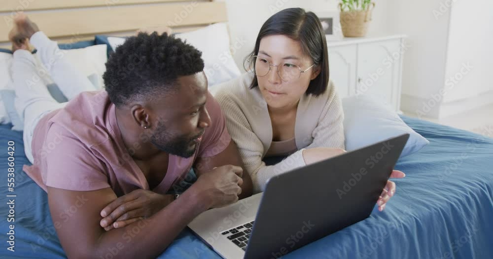 Happy diverse couple using laptop and lying in bedroom Happy diverse couple using laptop and lying in bedroom