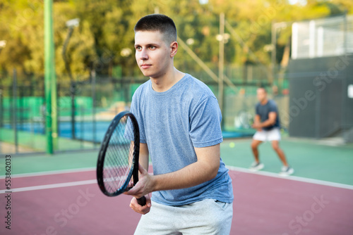 Portrait of sporty man standing with tennis racquet in his hands ready to play match in open court on summer day © JackF